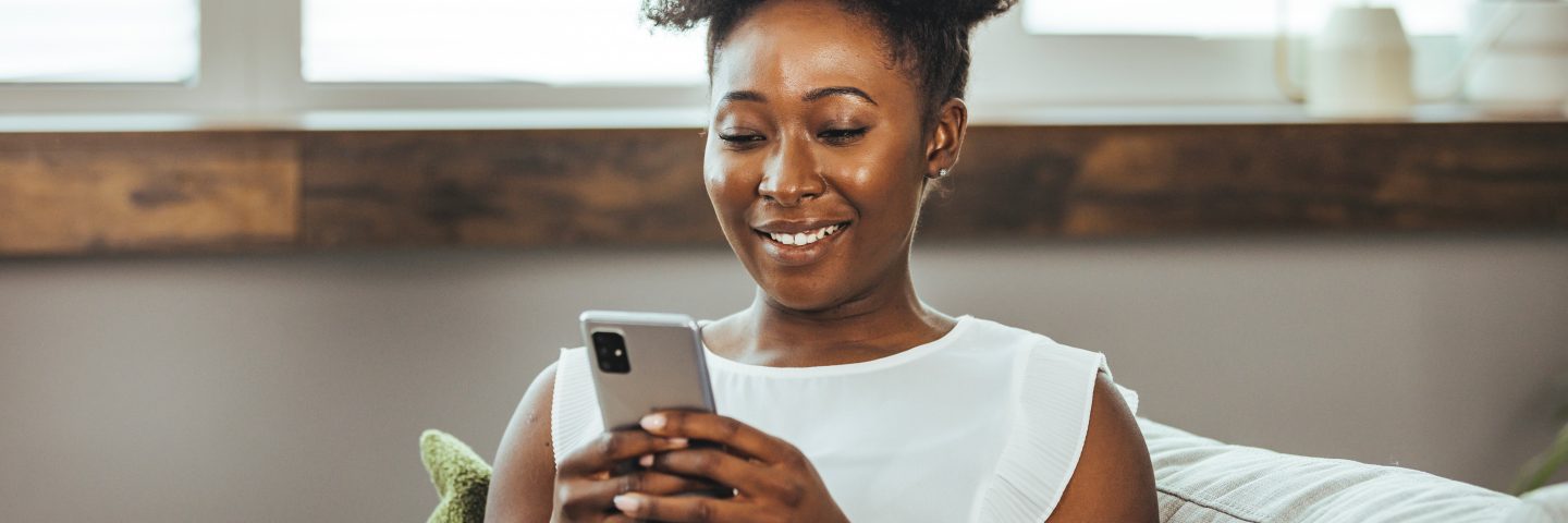 Cropped shot of an attractive young woman using her cellphone while sitting in the living room during the day. Keeping her social media fans updated