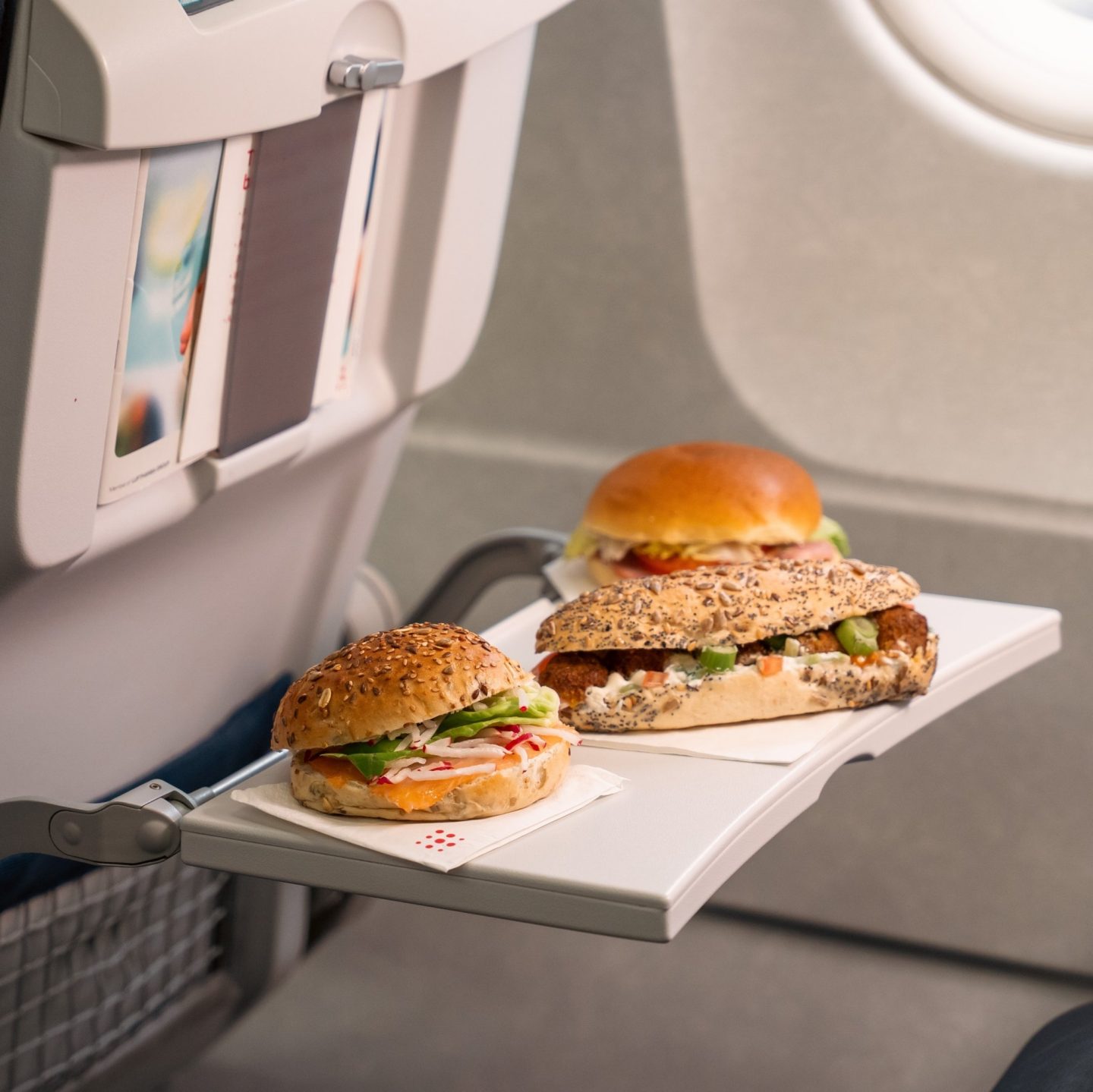 Two gourmet sandwiches on an airplane tray table.