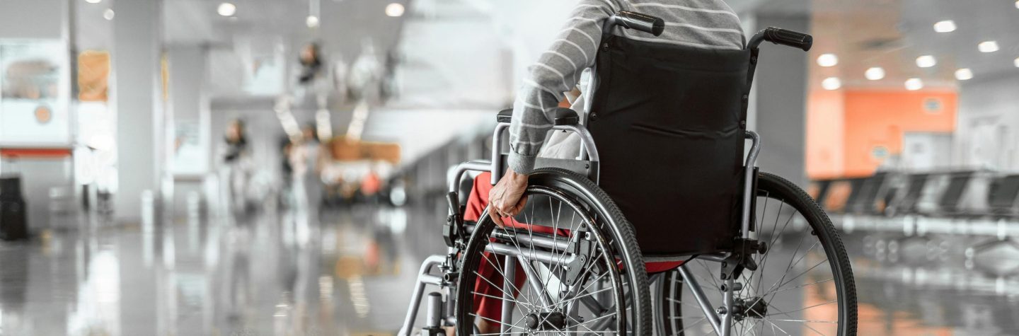 Back view photo of old woman moving in wheelchair in the lobby at airport. Copy space in left side