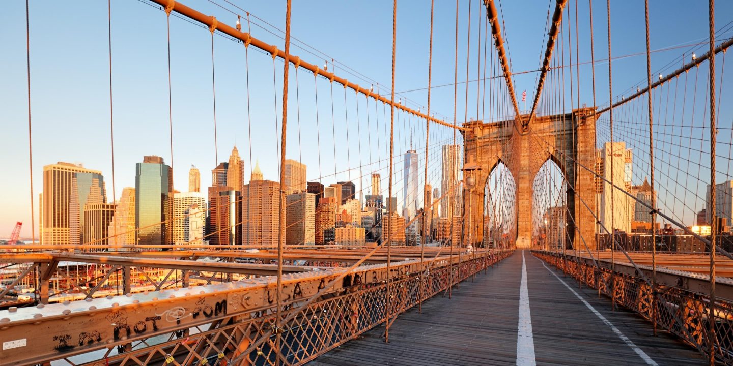 Brooklyn Bridge over East River viewed from New York City Lower Manhattan waterfront at sunset.