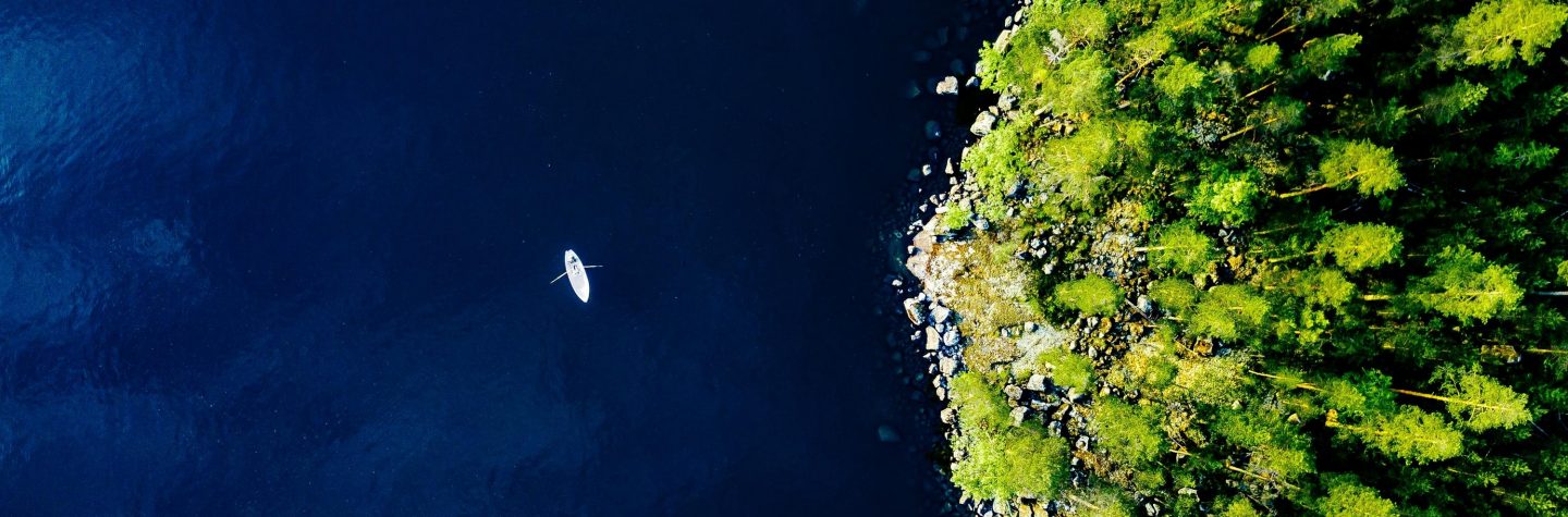 Aerial view of a boat sailing on a lake surrounded by a dense green forest.