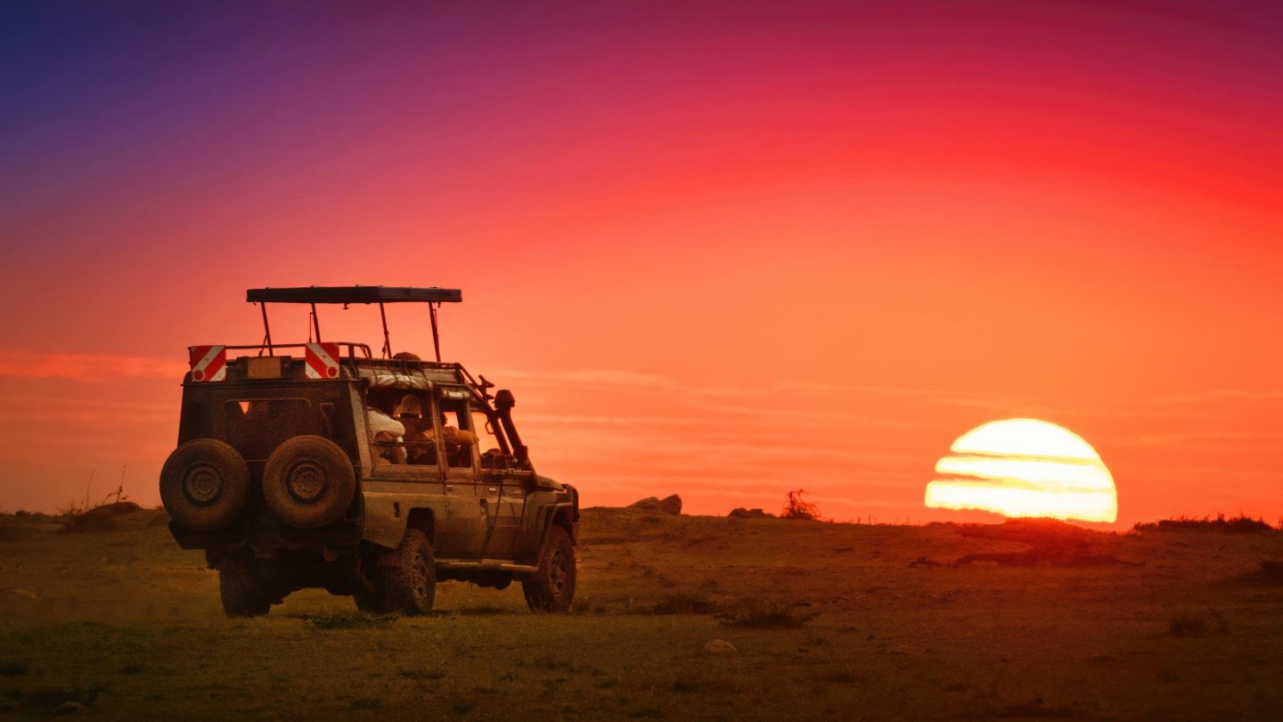 A safari vehicle with top up driving toward the rising sun on the horizon in Masai Mara, Kenya.
