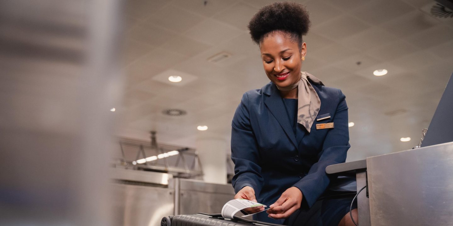 A woman at the airport holds a piece of paper, likely related to travel or corporate solutions.