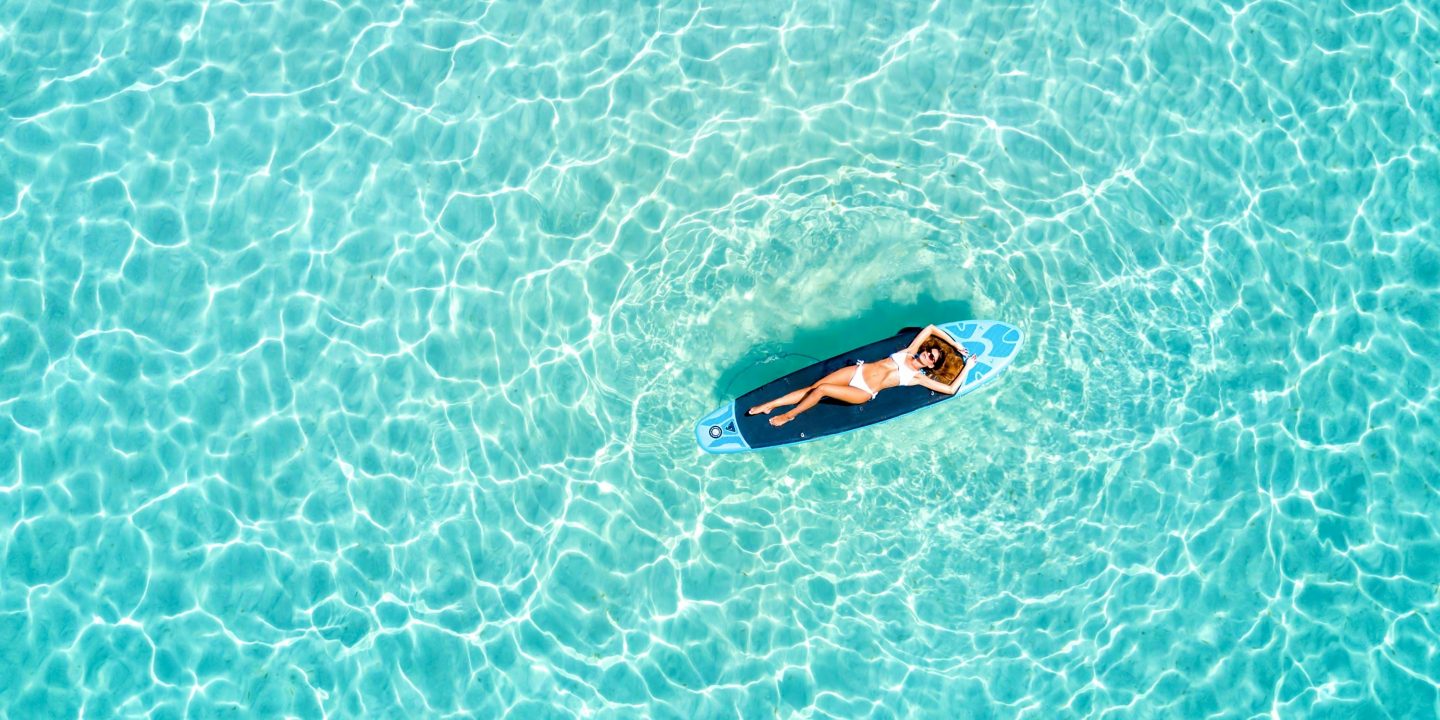 Woman in a bikini sunbathing on a surfboard in turquoise water.