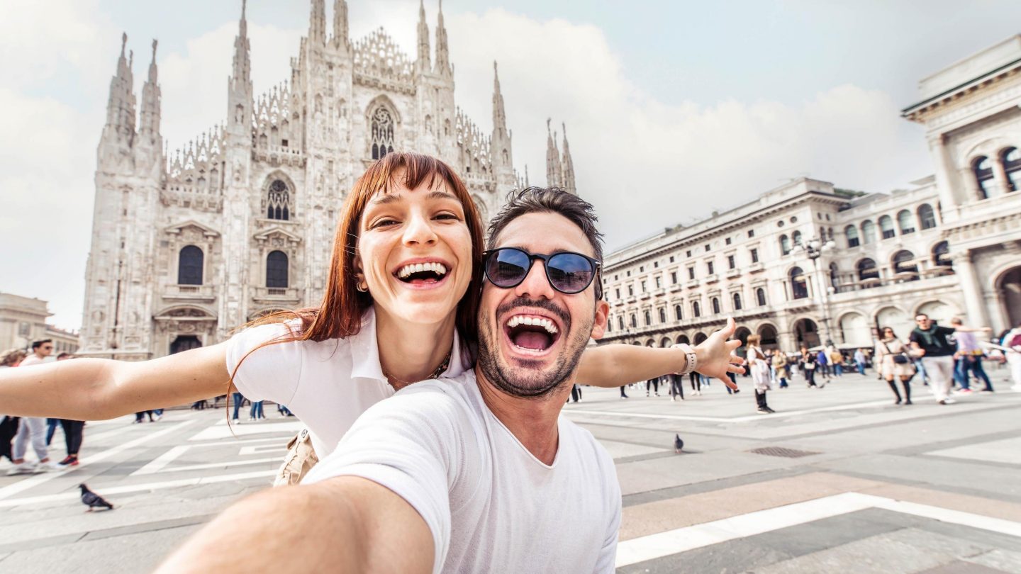 Happy couple taking selfie in front of Duomo cathedral in Milan, Lombardia - Two tourists having fun on romantic summer vacation in Italy - Holidays and traveling lifestyle concept