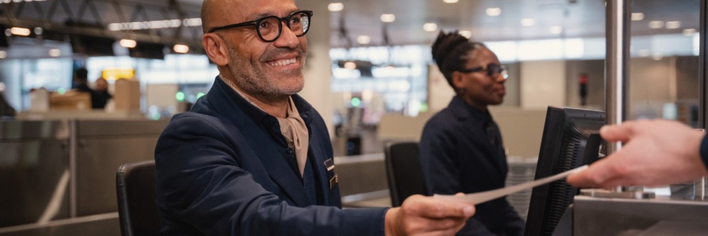 Smiling ground crew handing boarding pass at checking.