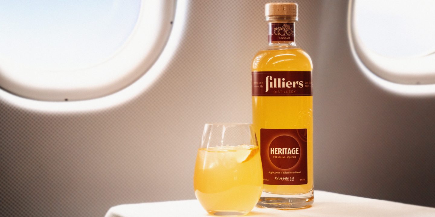 A bottle of Filliers spirit and a glass next to an airplane window.