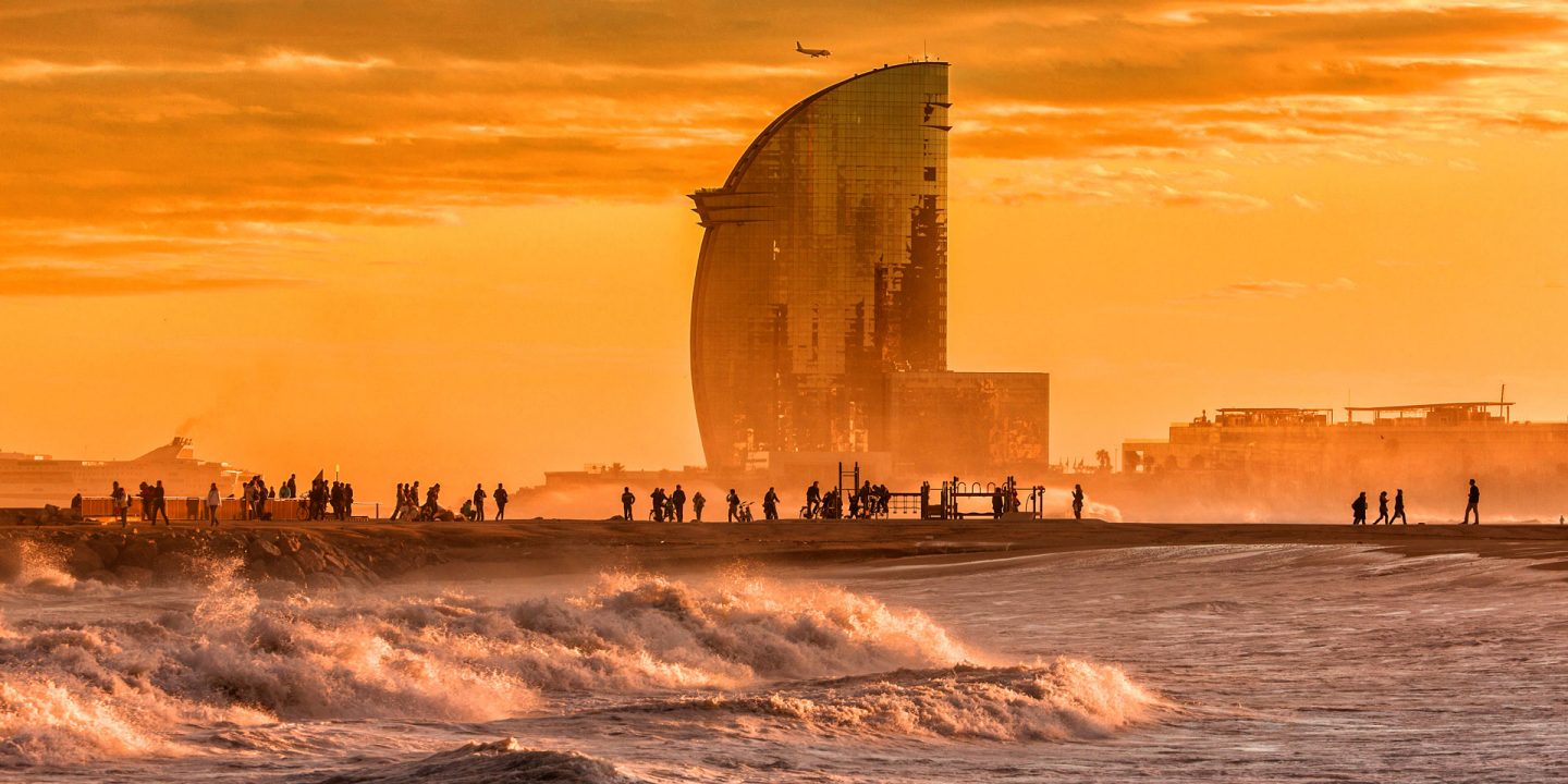 Uitzicht op Barcelona bij zonsondergang, met warm goudkleurig licht over de skyline van de stad en de Middellandse Zeekust.