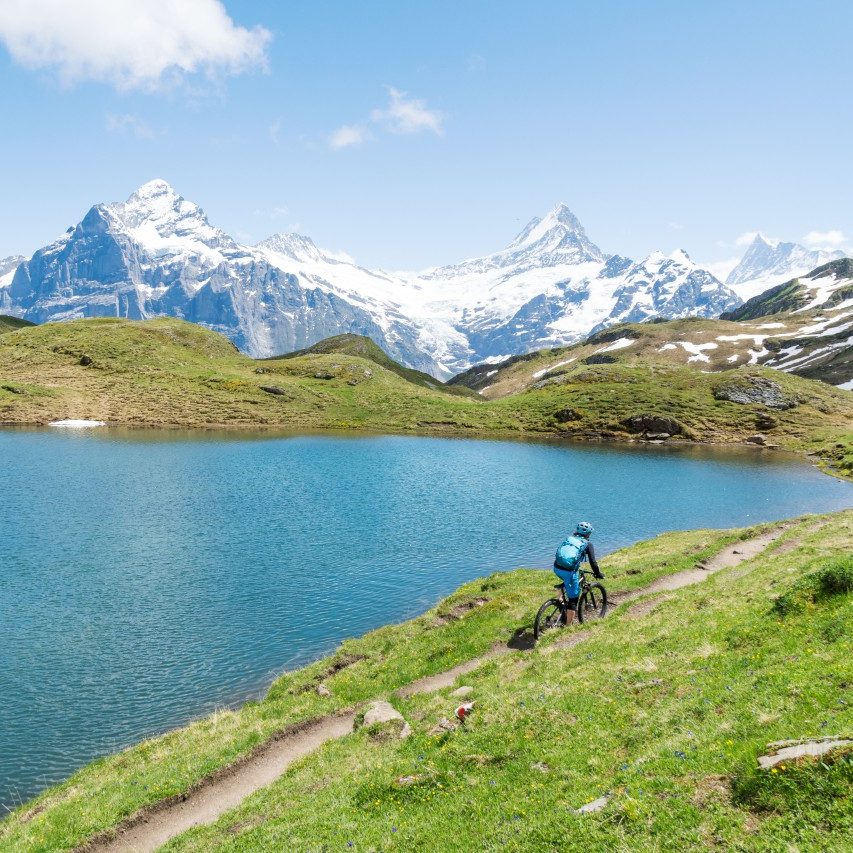 A cyclist riding on a mountain path next to an alpine lake.
