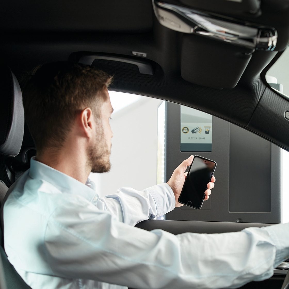 A man in a car scanning his smartphone at a parking terminal.