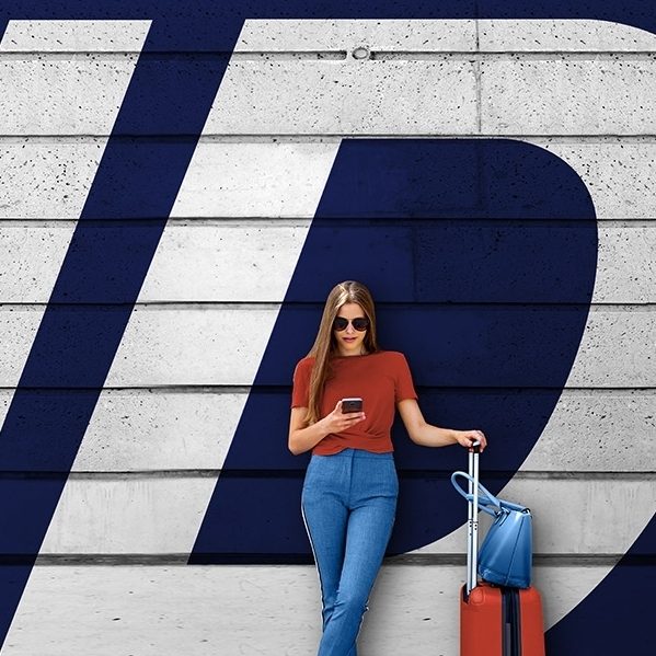 Woman with an orange suitcase and phone in front of a large Travel ID logo.