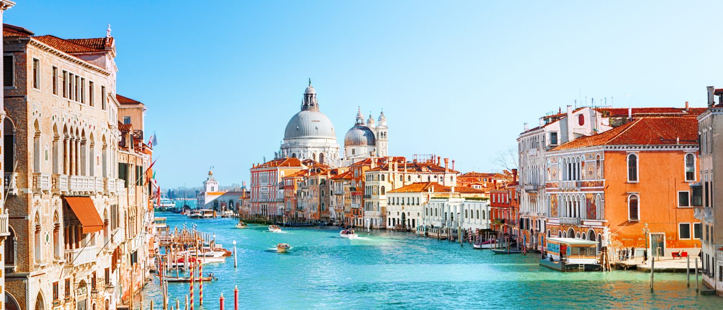Gondolas gliding along a picturesque canal in Venice on a sunny day.