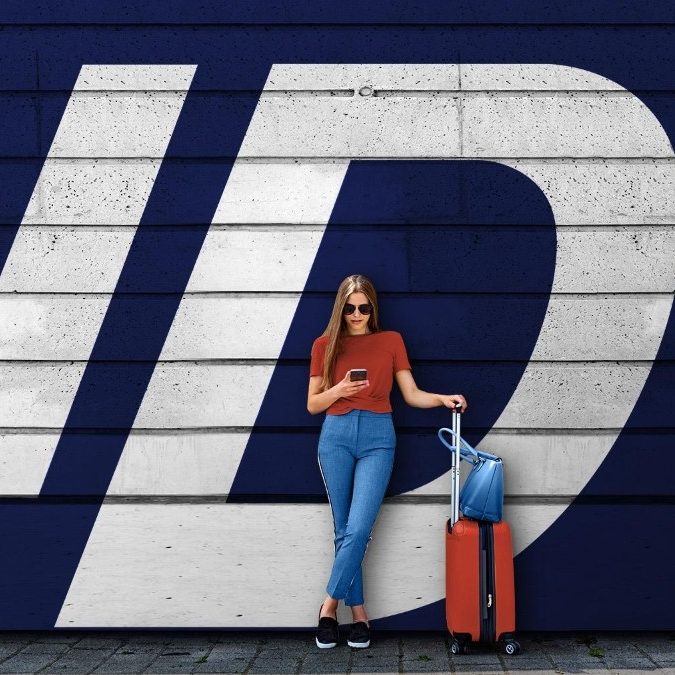 Woman with an orange suitcase and phone in front of a large Travel ID logo.