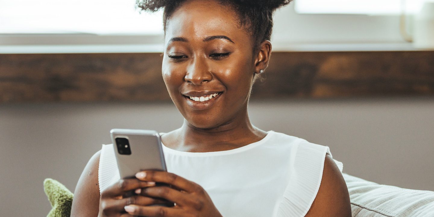 Cropped shot of an attractive young woman using her cellphone while sitting in the living room during the day. Keeping her social media fans updated