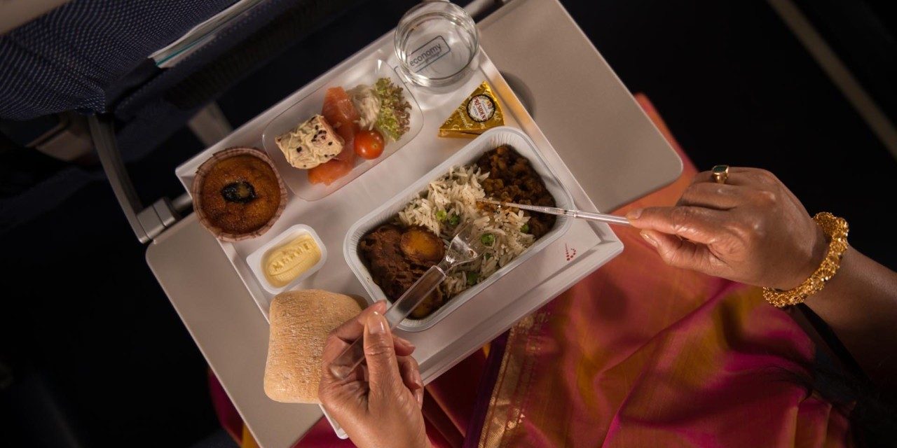 A passenger eating a hot inflight meal from a tray in Economy Class.