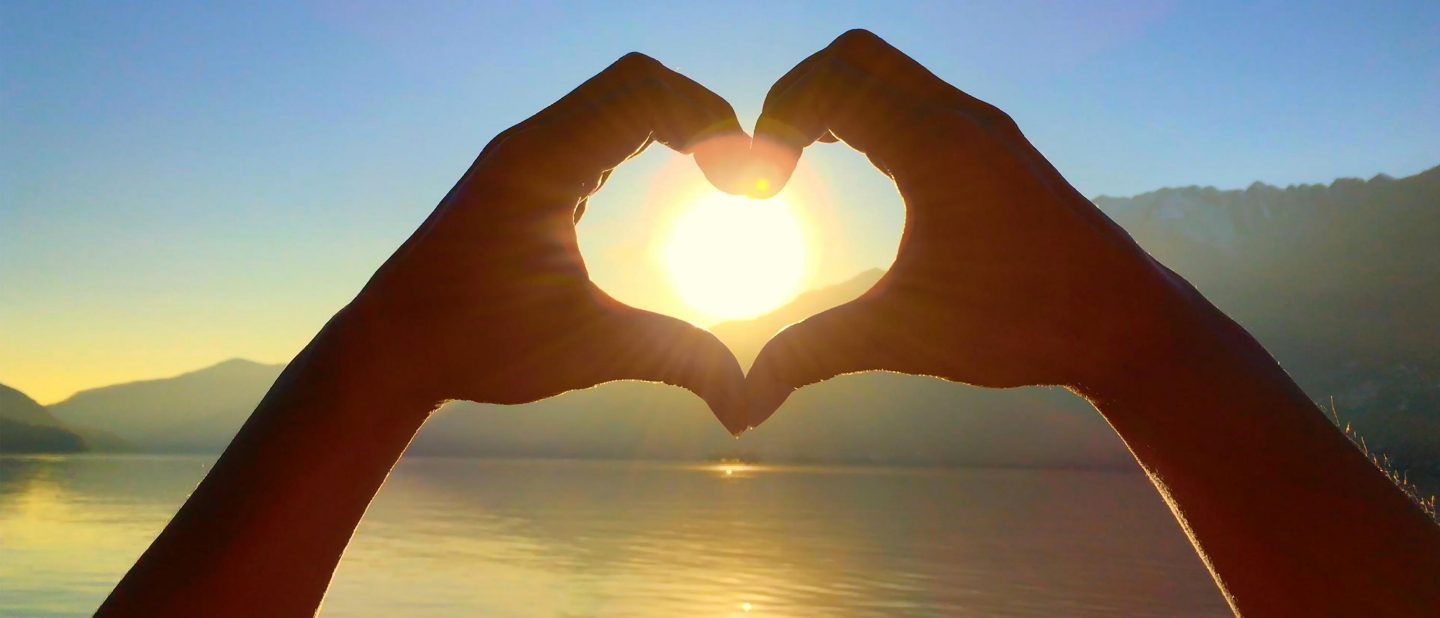 Hands forming a heart shape against a bright sunlit background.